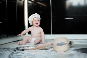 weinig jongen zittend Aan tapijt in keuken spelen met Koken potten. schattig jongen Koken in keuken Bij huis foto