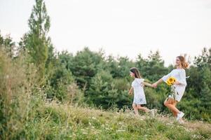 vrolijk moeder en haar weinig dochter hebben pret samen in de zomer achtergrond. gelukkig familie in de natuur achtergrond. schattig meisjes met kleurrijk bloemen foto