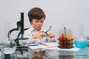 de jongen met een microscoop en divers kleurrijk kolven Aan een wit achtergrond. een jongen aan het doen experimenten in de laboratorium. explosie in de laboratorium. wetenschap en onderwijs foto