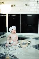 weinig jongen zittend Aan tapijt in keuken spelen met Koken potten. schattig jongen Koken in keuken Bij huis foto