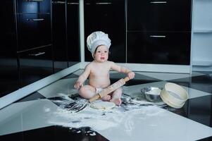 weinig jongen zittend Aan tapijt in keuken spelen met Koken potten. schattig jongen Koken in keuken Bij huis foto