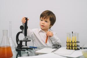 de jongen met een microscoop en divers kleurrijk kolven Aan een wit achtergrond. een jongen aan het doen experimenten in de laboratorium. explosie in de laboratorium. wetenschap en onderwijs foto