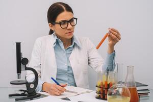 mooi medisch artsen in handschoenen en bril zijn werken met stoffen in test buizen en microscoop Bij de laboratorium. foto van aantrekkelijk geconcentreerd vrouw dokter schrijven voorschrift Aan speciaal het formulier