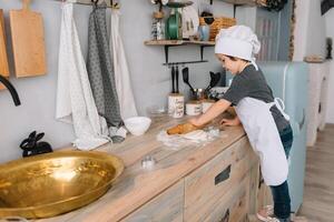 jong gelukkig mam en haar baby koken koekjes Bij huis in de keuken. Kerstmis eigengemaakt ontbijtkoek. schattig jongen met moeder in wit uniform en hoed gekookt chocola koekjes. foto