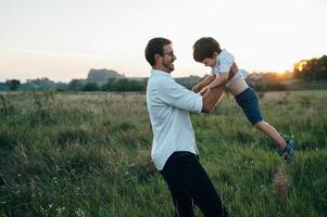 knap vader met zijn weinig schattig zoon zijn hebben pret en spelen Aan groen met gras begroeid gazon. gelukkig familie concept. schoonheid natuur tafereel met familie buitenshuis levensstijl. familie resting samen. vaders dag. foto