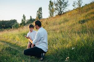 knap vader met zijn weinig schattig zoon zijn hebben pret en spelen Aan groen met gras begroeid gazon. gelukkig familie concept. schoonheid natuur tafereel met familie buitenshuis levensstijl. familie resting samen. vaders dag. foto