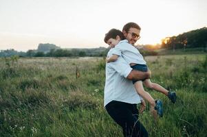 knap vader met zijn weinig schattig zoon zijn hebben pret en spelen Aan groen met gras begroeid gazon. gelukkig familie concept. schoonheid natuur tafereel met familie buitenshuis levensstijl. familie resting samen. vaders dag. foto