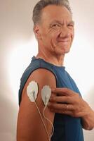 Mens gebruik makend van een elektro behandeling stimulator of tientallen eenheid Aan zijn deltaspier voor pijn Verlichting voor spieren en gewrichten foto