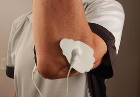 Mens gebruik makend van een elektro behandeling stimulator of tientallen eenheid Aan zijn elleboog voor pijn Verlichting van spieren en gewricht foto