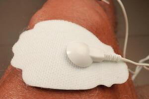 Mens gebruik makend van een elektro behandeling stimulator of tientallen eenheid Aan zijn knie voor pijn Verlichting van spieren en gewricht foto