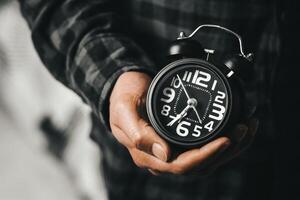 tijd beheer concept. Mens handen Holding zwart retro alarm klok. tijd naar wakker worden omhoog voor de ochtend- routine- foto