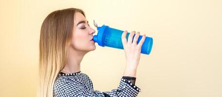 dorstig vrouw met blauw plastic fles tegen een licht achtergrond. een mooi jong Kaukasisch zakenvrouw in een blouse drinken water Aan geel. foto