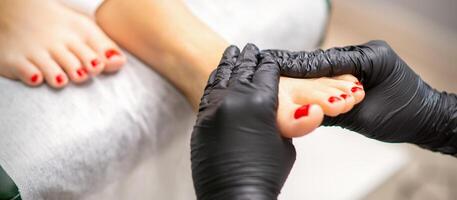 voet massage met hydraterend en pellen room door pedicure handen vervelend zwart handschoenen, dichtbij omhoog. foto