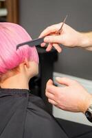 handen van kapper kammen haar- maken kort roze kapsel voor een jong Kaukasisch vrouw in een schoonheid salon. foto