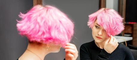 mooi jong Kaukasisch vrouw op zoek Bij haar kort roze haar- in een spiegel. foto