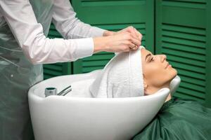 een kapper is omhulsel een vrouw hoofd in een handdoek na het wassen haar- in de schoonheid salon. foto