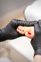 voet massage met hydraterend en pellen room door pedicure handen vervelend zwart handschoenen, dichtbij omhoog. foto