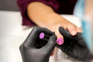 schilderij nagels van een vrouw. handen van manicure in zwart handschoenen toepassen roze nagel Pools Aan vrouw nagels in een schoonheid salon. foto