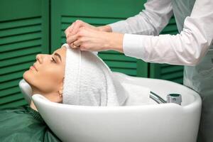 een kapper is omhulsel een vrouw hoofd in een handdoek na het wassen haar- in de schoonheid salon. foto