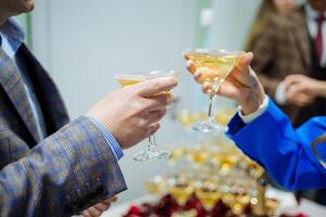 een Mens en een vrouw gerinkel bril van Champagne, een alcohol partij, een geslacht partij, echtgenoten vieren een verjaardag, wit sprankelend wijn, een driehoekig glas voor drinken. foto