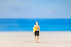 miniatuur mensen Mens in een zwempak, en Holding een geel surfboard Aan de strand foto