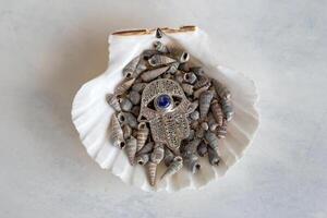 een verbijsterend zilver hamsa hand- met een betoverend blauw onheil oog charme, vertegenwoordigen bescherming, weergegeven tegen een rustig achtergrond van delicaat wit schelpen. foto