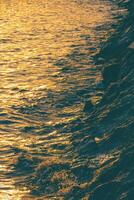 mooi gouden zonlicht reflectie Aan zee oppervlakte met rots stapel langs de strand Bij zonsondergang tijd in verticaal kader foto