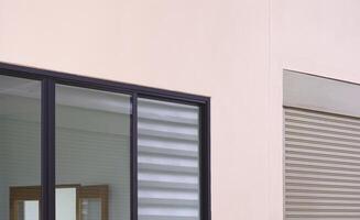 glas glijden ramen en rol Luik deur Aan beige beton muur van industrieel kantoor gebouw, perspectief kant visie foto