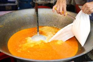 Koken Thais kerrie voedsel . gieten de kokosnoot melk in de gouden oranje kerrie in de pan foto