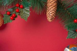 Kerstdecoratie en dennentakken krans met kersen en dennenappel op rode tafel foto