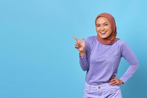 portret van glimlachende jonge aziatische vrouw die met de vinger wijst naar kopieerruimte op blauwe achtergrond foto
