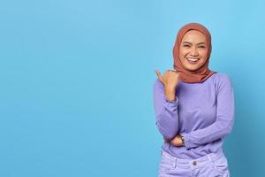 portret van glimlachende jonge aziatische vrouw die een duim richt op kopieerruimte op blauwe achtergrond