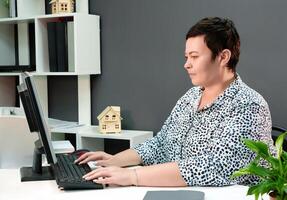 leiderschap positie. een zelfverzekerd en bekwaam brunette meisje met een kort kapsel zit achter een bureau in een modern kantoor, effectief beheren projecten en coördineren werk via computer foto