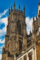 gotisch kathedraal toren tegen een blauw lucht met wolken, presentatie van ingewikkeld bouwkundig details en vliegend steunberen in york, noorden yorkshire, Engeland. foto