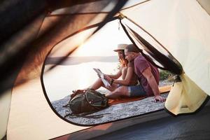 uitzicht vanuit tent van paar met kaart liggend op het meer tijdens wandeltocht. avel lifestyle concept avontuurlijke vakanties buiten foto