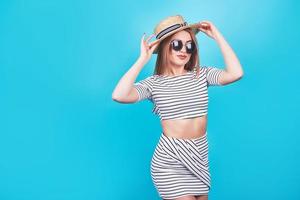 aantrekkelijk meisje in een witte en zwarte strepen, hoed, zonnebril, emotioneel geopende mond op een helderblauwe achtergrond met een perfect lichaam. geïsoleerd. studio opname foto