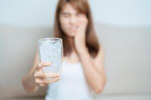 tanden gevoelig naar verkoudheid concept. vrouw houden ijs water glas en hebben kiespijn en pijn na eten. tand verval of gom ziekte, slijpen tanden en spanning, blootgesteld zenuw wortels, barst en terugwijkend tandvlees foto