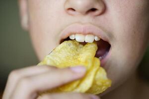 Bijsnijden onherkenbaar meisje aan het eten knapperig aardappel chips foto