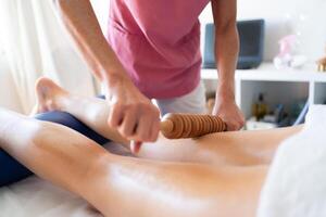 Bijsnijden masseuse aan het doen houten apparaat massage naar been van cliënt foto