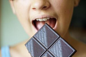 anoniem tiener- meisje met mond breed Open aan het eten chocola bar foto