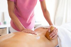 Bijsnijden masseur aan het doen massage naar cliënt met houten behandeling gereedschap in fysiotherapie kliniek foto