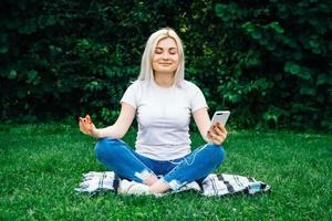 vrouw in koptelefoon en smartphone in handen op groen gras