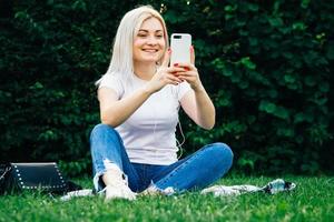 vrouw in koptelefoon en smartphone op groen gras foto