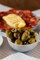 een schotel van levendig groen olijven is reeks tegen een backdrop van traditioneel alentejo kaas en genezen worst. de tafereel vangt de essence van Portugees keuken in een knus restaurant instelling. foto