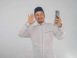 Moslim Aziatisch Mens golvend hand- met gelukkig gezicht wanneer aan het doen telefoontje met zijn familie foto
