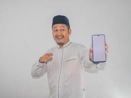 Moslim Aziatisch Mens glimlachen en richten naar blanco mobiel telefoon scherm dat hij houden foto