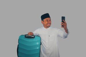 Moslim Aziatisch Mens draag- koffer tonen gelukkig uitdrukking wanneer op zoek zijn telefoon foto