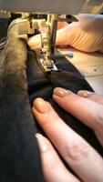 werkwijze van naaien in een naaien machine naaien vrouw handen manicure zwart textiel denim jeans fabricage dichtbij omhoog naaister in werkplaats kleding stof kleren maken ontwerp hobby handgemaakt werken handwerk foto