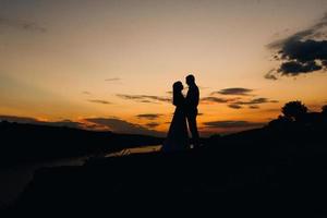 silhouetten van een gelukkig jong stel, jongen en meisje op een achtergrond van oranje zonsondergang foto