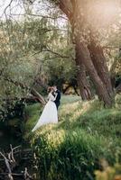 de bruidegom en de bruid wandelen in het bos bij een smalle rivier foto